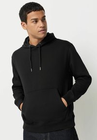 Sort hættejakke med snore, frontlomme, ribbede manchetter og kant. Lavet af glat stof, tætsiddende design og minimalistisk stil.