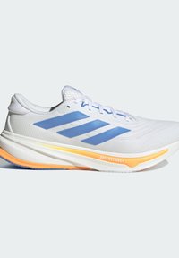 Zapatilla de running blanca con rayas azules de Adidas y acento naranja en la suela, etiquetada como "DREAMSTRIKE+" sobre un fondo liso.