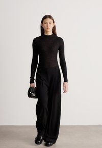 Sieviete, valkājot piegulošu melnu riboto džemperi, plašas melnas bikses, melnas kurpes un tur mazu melnu roku somiņu, soļo uz priekšu.