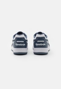 Pár bílých a námořnických tenisek Reebok zobrazených zezadu na čistém bílém pozadí.
