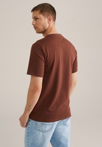 Braunes Kurzarm-T-Shirt aus weichem Stoff, mit klassischer Passform und rundem Ausschnitt, kombiniert mit hellblauen Denim-Jeans.