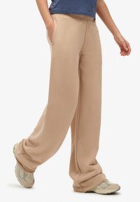 Beżowe spodnie dresowe o szerokich nogawkach wykonane z miękkiego materiału, z bocznymi kieszeniami i luźnym krojem. W połączeniu z jasnymi butami sportowymi.