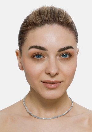 Collier ras du cou en argent tressé, présentant une surface lisse et texturée avec un design fluide et ondulé, porté sur un teint neutre.