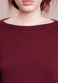 Maglione bordeaux con scollatura ampia, texture a coste e design aderente, adatto per un look casual.