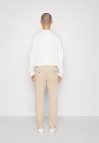 Cămașă albă cu mâneci lungi, pantaloni chino bej cu două buzunare la spate și adidași albi. Ținuta are linii simple și curate, cu o paletă de culori neutră.