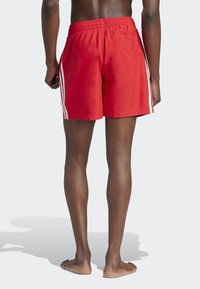 Κόκκινα μαγιό φτιαγμένα από ελαφρύ υλικό. Διαθέτουν ελαστική μέση, δύο λευκές πλευρικές ρίγες και άνετη εφαρμογή. Ίσια μύτη στο κάτω μέρος.