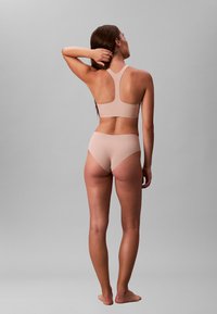 Nøddefarvet sports-bh og bikini sæt med en glat tekstur; racerback-design og mellemhøj talje; få sømme og blød finish.