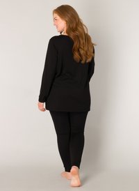 Zwarte tuniek met lange mouwen en aansluitende leggings van zachte stof, met een ruime pasvorm en een gladde textuur, blote voeten.