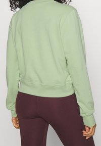 Sudadera de color verde claro con un cuello redondo y puños acanalados; combinada con leggings de color burdeos oscuro, mostrando un diseño de atuendo casual.