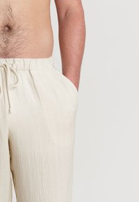Pantalons en lin à coupe décontractée, couleur beige clair, taille élastique, fermeture à cordon et deux poches latérales.