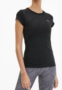 Svart tränings t-shirt med korta ärmar, utrustad med ett texturerat geometriskt mönster på den övre framsidan. Slät tyg, åtsittande design.