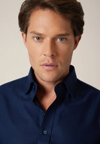 Ciemnoniebieska koszula na guziki z kołnierzem typu spread, gładką teksturą i regularnym krojem; posiada dwa guziki na kołnierzu i staranne przeszycia.