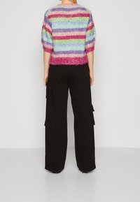Meer gekleurd gestreepte trui met een pluizige textuur en korte mouwen, gecombineerd met hooggetailleerde zwarte cargobroek met zijzakken.