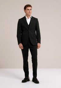 Melns uzvalks ar vienas krūts žaketi un iegrieztiem atlokiem, kombinēts ar baltu kaki kreklu un atbilstošām melnām biksēm. Gluda auduma, pielāgota piegriezuma.