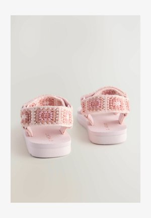 Lyserøde sandaler med et vævet remdesign, som har blødt, tekstureret stof og en støttende, flad plastsål.