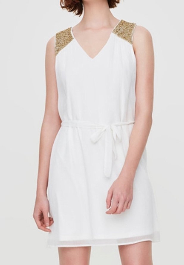 Robe blanche sans manches avec décolleté en V, détails aux épaules en sequins dorés et ceinture nouée à la taille portée par une personne aux cheveux courts.