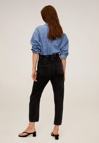 Chemise en denim bleu clair avec les manches retroussées, associée à un jean noir taille haute avec poches latérales, portée avec des sandales noires.
