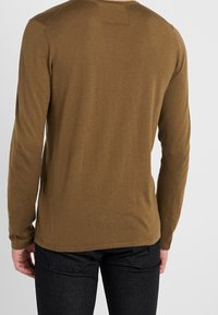 Braunes Langarmhemd aus weichem Stoff, mit rundem Ausschnitt und lockerer Passform, mit minimalen Nahtdetails auf der Rückseite.