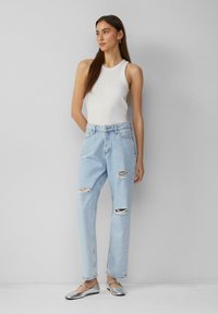 Haut sans manches blanc avec des détails en strass, associé à un jean léger bleu déchiré et des chaussures plates en argent. Design de tenue simple et décontractée.