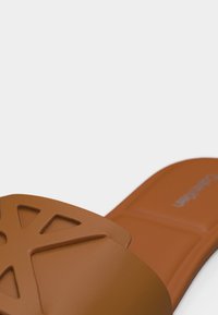 Sandale à glissière marron avec un design découpé géométrique sur la bride et une semelle intérieure texturée, présentée sur un fond blanc.