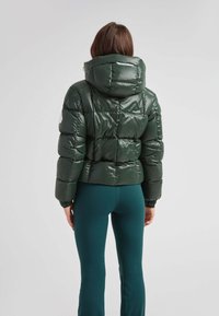 Grøn pufferjakke med en blank finish, cropped design, oversized hætte og quiltet tekstur. Parret med tætsiddende teal leggings.