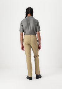 Short-sleeve gray shirt and beige trousers, showing a tailored fit. Clean lines with a back pocket detail, paired with black shoes.
