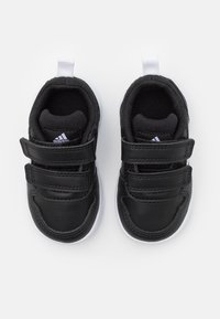 Zapatillas negras con upper de cuero sintético, dos correas de Velcro, suela de goma blanca y forro interior texturizado. Presenta el logo de Adidas.