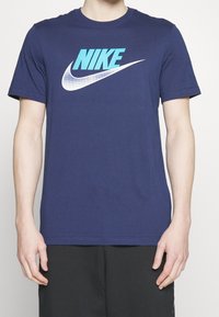 Marinblå bomull t-shirt med en stor turkos "NIKE"-logga och en vit swoosh. Korta ärmar och en klassisk rundad halsringning.