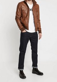 Brown leather bomber jacket with two front pockets, white graphic t-shirt, dark denim jeans with rolled cuffs, and black ankle boots.