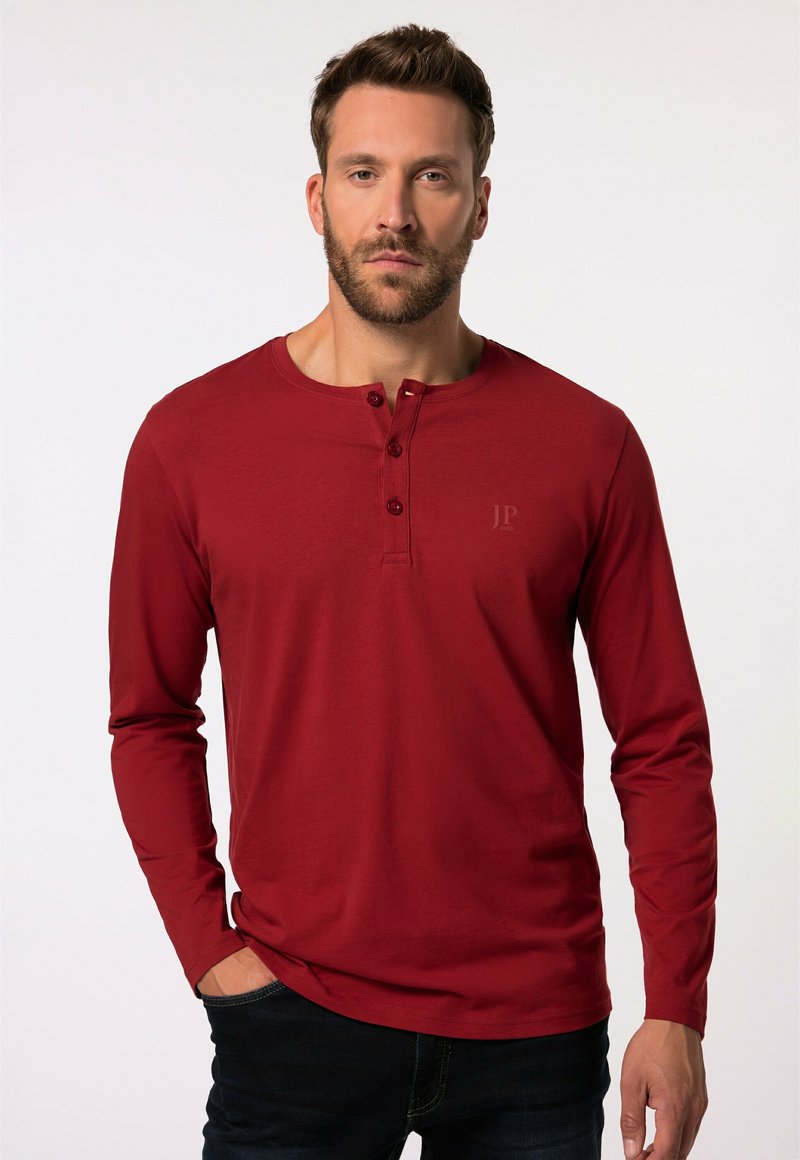 Maglietta henley rossa a maniche lunghe con tre bottoni al collo, realizzata in un tessuto morbido. Presenta un logo sottile sul petto e un design aderente.