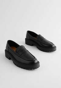 Black leather loafers with a chunky platform sole and textured detailing on the toe. Smooth surface with a sleek, rounded design.