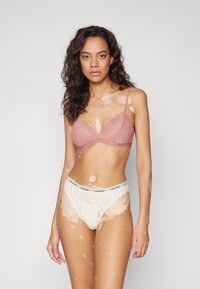 Sutien din dantelă în nuanța trandafirului prăfuit, cu bretele reglabile, și chilot din dantelă crem asortat, cu talie logo Calvin Klein, având detalii cu model de piele.