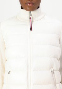 Hvid puffervest med høj hals, lynlås og ribbede detaljer. Kendt for sin quillede tekstur og sidelommer.