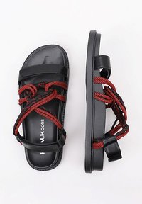 Sandalias negras con detalles de cuerda trenzada roja, con suelas planas y correas anchas. Textura suave con una correa ajustable en la parte trasera.