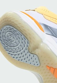 Semelle de chaussure de sport blanche avec un motif en spirale en caoutchouc bleu clair, des accents orange et des zones texturées marron clair pour l'adhérence.