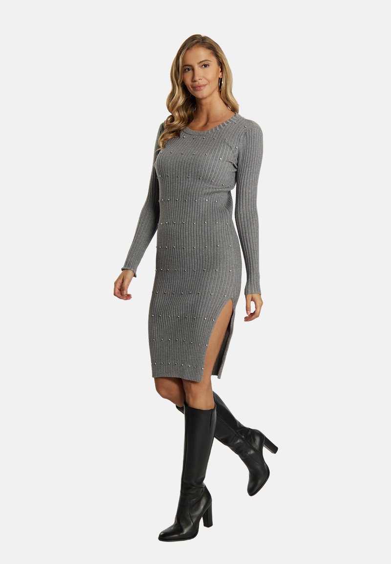 Graues geripptes Kleid mit langen Ärmeln, seitlichen Schlitzen und Verzierungen. Getragen mit schwarzen knieh hohen Stiefeln, die eine enganliegende Silhouette haben.