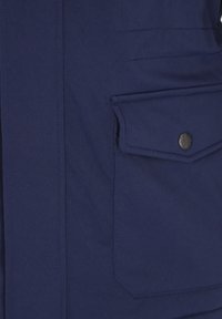 Tela de chaqueta azul oscuro con un bolsillo con solapa asegurado por un botón metálico redondo en el lado derecho.