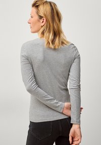 Grijze langwerpige shirt met lange mouwen in zachte stof, strakke pasvorm, met een ronde halslijn en slanke mouwen. Gecombineerd met donkere jeans, gezien vanuit de achterkant.