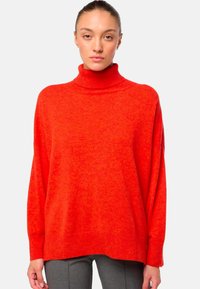 Pull en col roulé rouge avec une coupe oversize, tissu texturé, col et poignets côtelés, et design à épaule tombante.