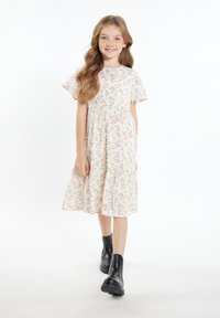 Knee-length Kleid mit Blumenmuster in Creme, kurzen Rüschensleeves und gerafftem Tailleneinsatz. Tragen mit schwarzen Knöchelstiefeln.