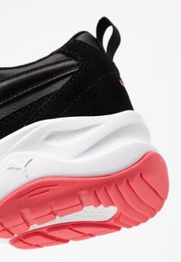 Černá bota s patou a bílou mezipodešví a červenou texturovanou podrážkou, vybavená poutkem a jemným logem Puma na straně.