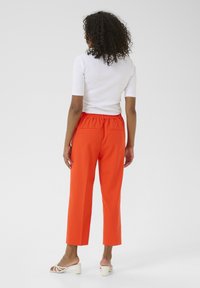 Pantaloni arancioni a vita alta e gamba larga con una cintura elastica, dotati di due tasche posteriori. Abbinati a un top aderente bianco e sandali.