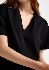 Czarny t-shirt z dekoltem w serek i krótkimi rękawami, wykonany z miękkiej tkaniny. Posiada luźny krój i gładką fakturę. Prosty design bez wzorów.