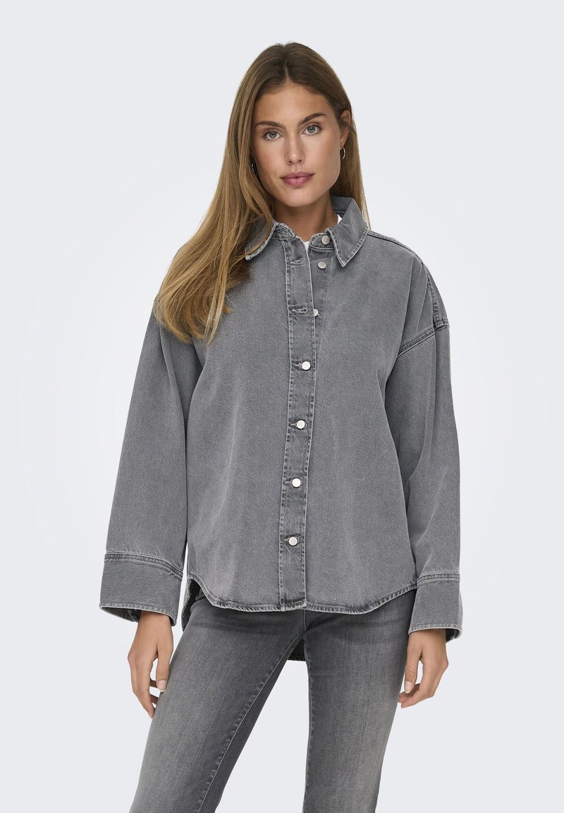 Camicia in denim grigio con chiusura a bottoni, colletto appuntito, spalle abbassate e vestibilità rilassata. Presenta bottoni in tonalità argento e dettagli cuciti.