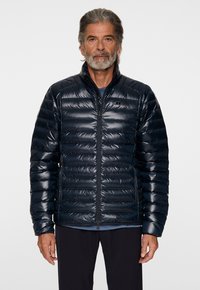 Tummansininen puhvitakki kiiltävällä pinnalla, tikattu muotoilu, korkea kaulus, etuvetoketju ja raglan-hihat. Sopii ulkoiluun.