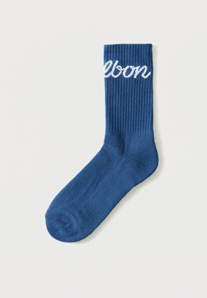 Chaussette bleue côtelée unique avec un texte en écriture cursive blanche près du haut indiquant "lebon" sur un fond blanc uni.