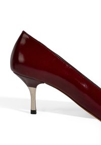 Escarpin en cuir verni bordeaux avec un talon en métal argenté mince. La chaussure présente un bout pointu et une texture lisse et brillante.