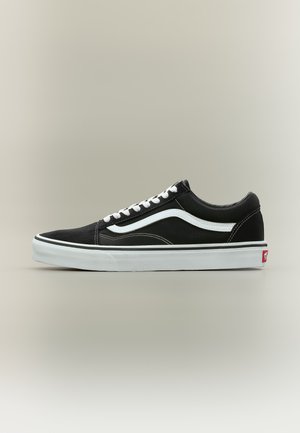Zapatilla negra de corte bajo con franja blanca lateral, cordones blancos y suela de goma blanca, mostrada de lado sobre un fondo neutro.