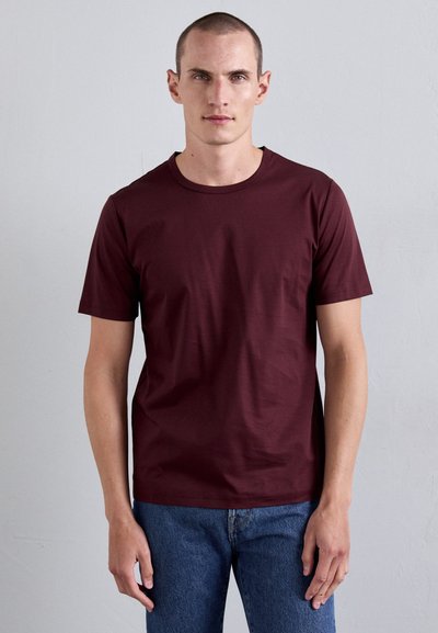 Burgunderrotes Baumwoll-T-Shirt mit Rundhalsausschnitt und kurzen Ärmeln. Einfaches, figurbetontes Design mit glatter Textur. Kombiniert mit blauen Jeans.