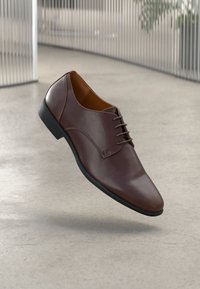 Hnědé kožené společenské boty s kulatou špičkou, hladkým povrchem a černou gumovou podrážkou. Obsahují šněrovací design a minimalistické detaily šití.